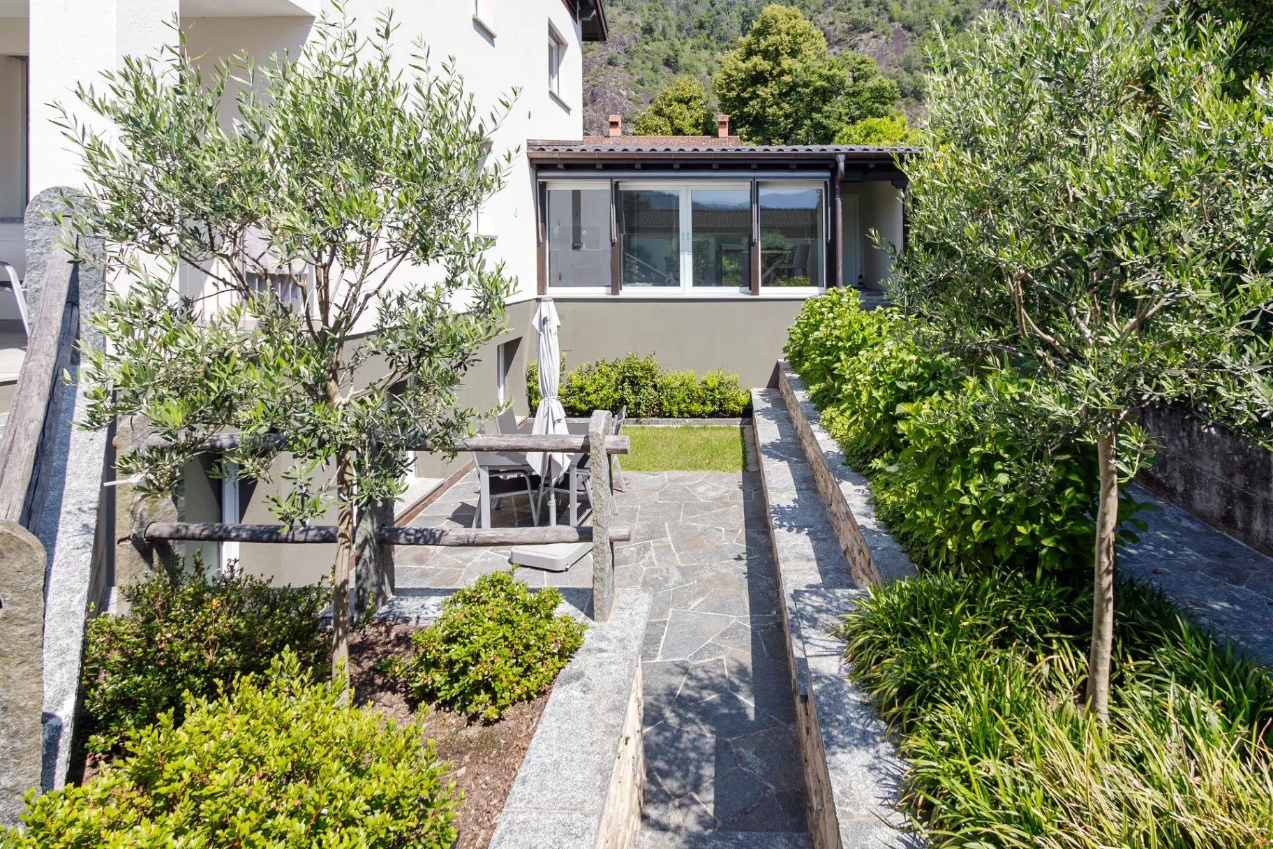Isorno Terrasse mit Esstisch, Sonnenschirm und Garten mit Olivenbäumen